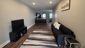 A modern living room with a flat-screen TV, a black sofa, a patterned rug, and a small side table. - Legacy Executive Retreat (Clarksville)