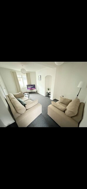 Una sala de estar moderna con dos sofás color beige, un televisor de pantalla plana y una pequeña mesa con una planta.