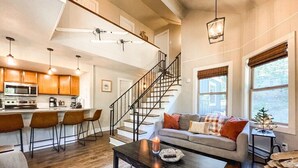 A modern kitchen with a microwave, stove, and bar stools. A staircase leads to a living area with a sofa and a coffee table. - 193 Range (Breckenridge)
