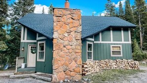 A two-story house with a stone chimney, green siding, and a stack of firewood outside. - 193 Range (Breckenridge)