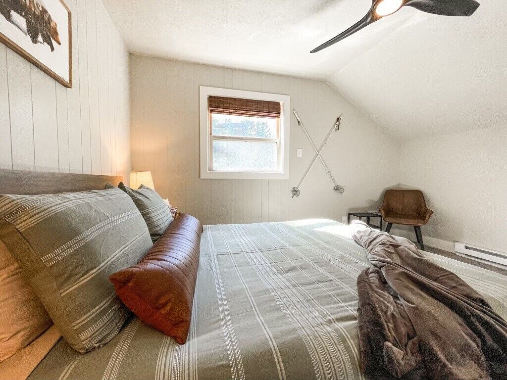 Ein Schlafzimmer mit Bett, Kissen, einem Fenster, einem Deckenventilator und einem Stuhl.