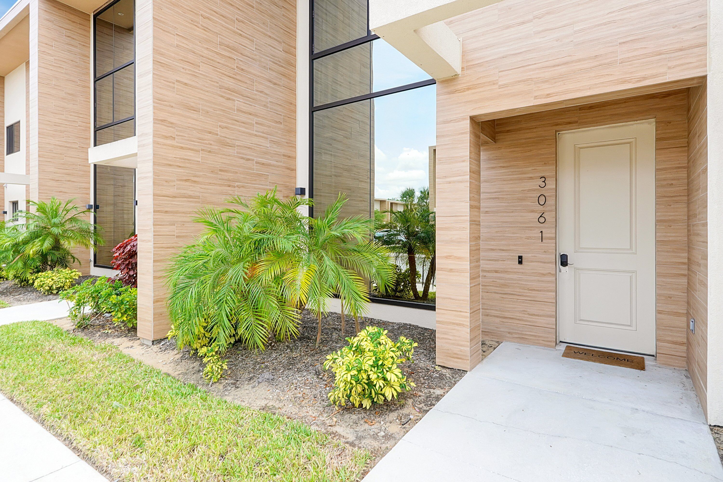 A modern building with a clean, minimalist design, featuring a large glass window, a welcoming door with a number, and a well-maintained garden area.