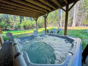 Ein Whirlpool unter einer hölzernen Pergola mit einer Rasenfläche und Bäumen im Hintergrund.