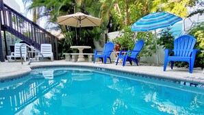 Una piscina con sillas y sombrillas azules, rodeada de vegetación.