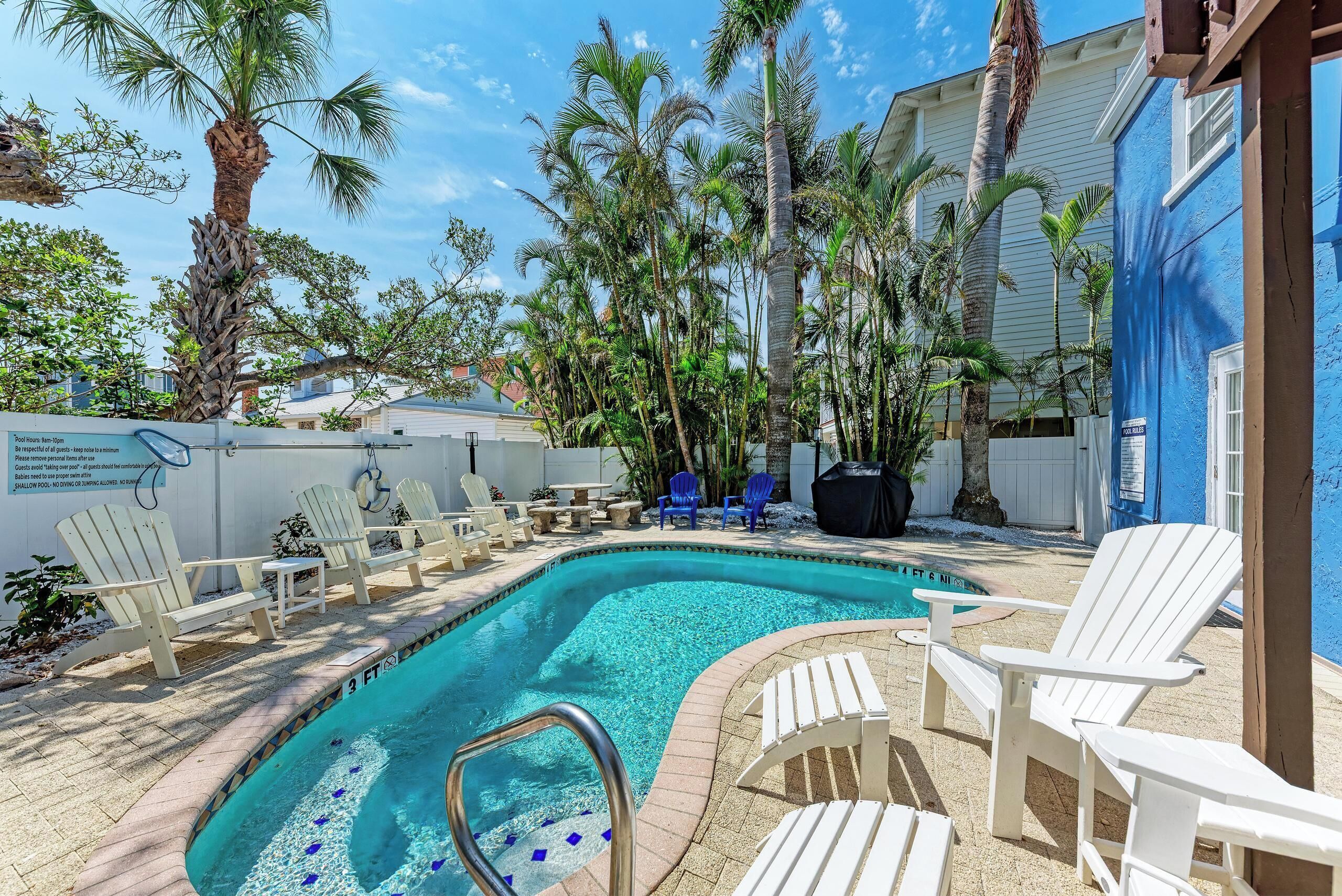 A pool area with white lounge chairs, a shallow pool, and palm trees.