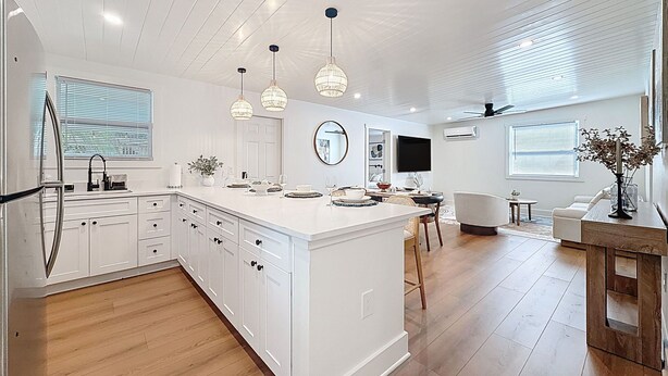 A modern kitchen with white cabinetry, a central island, pendant lighting, and a dining area with a white sofa and table. - 3716 7th Ave W (Bradenton)