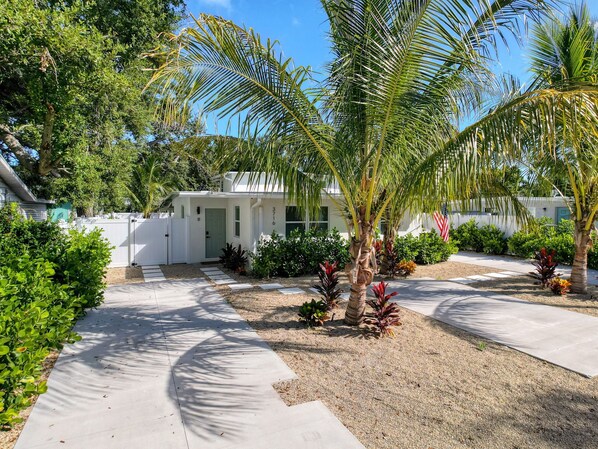 A white house with a covered porch, surrounded by a gravel driveway and various tropical plants. - 3716 7th Ave W (Bradenton)