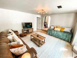 Un salon avec un canapé marron, une table basse en bois, un canapé vert avec des coussins à motifs et un téléviseur.