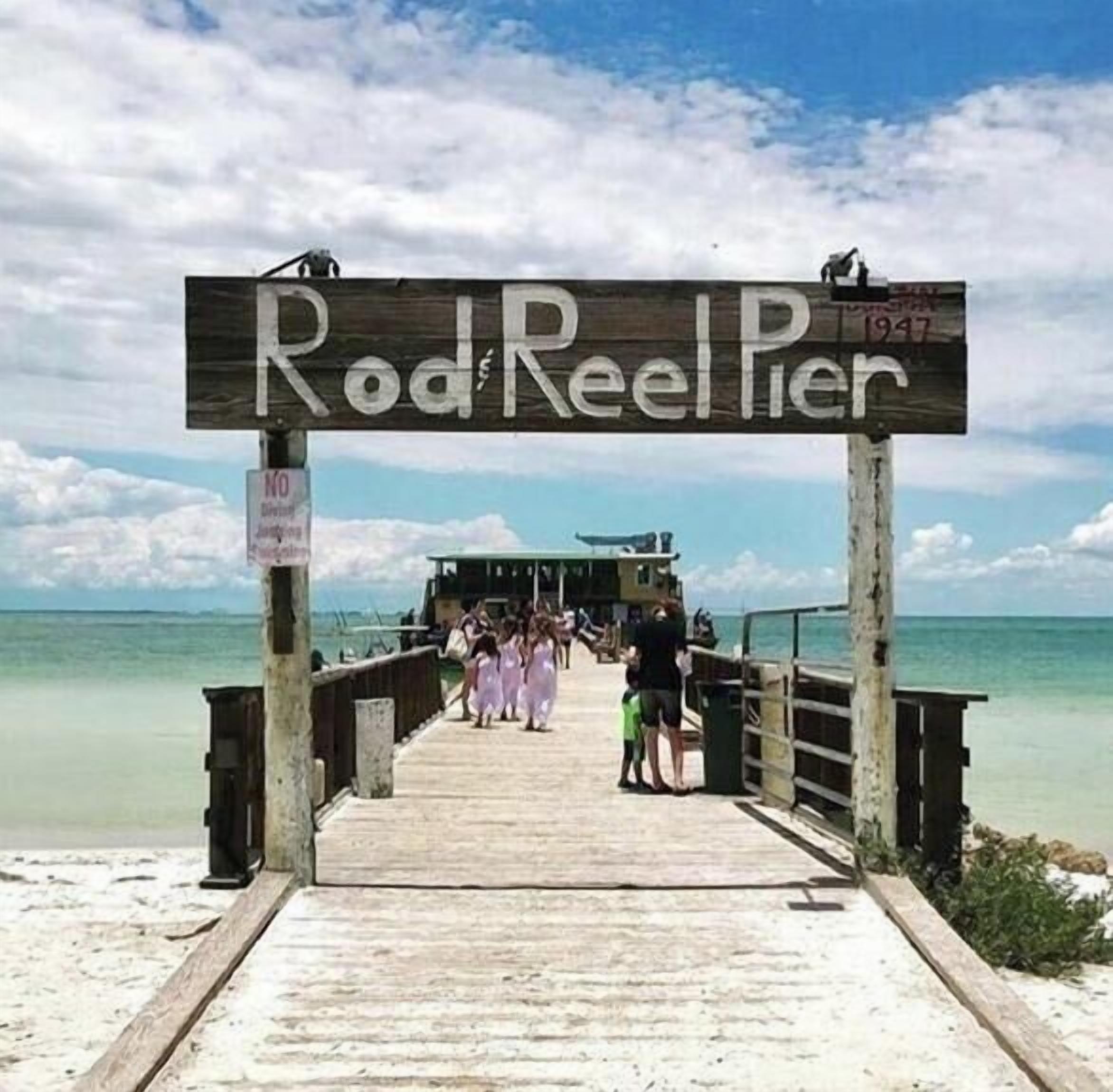 A wooden pier leading to Rod Reel Pier with a clear view of the ocean and a small building at the end.