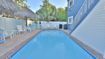 A swimming pool with a 3 FT depth marker, surrounded by white chairs and a covered grill area.