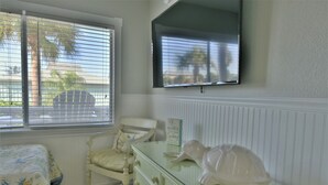 Een slaapkamer met een bed, een kaptafel, een stoel, een aan de muur bevestigde televisie en een raam met jaloezieën.