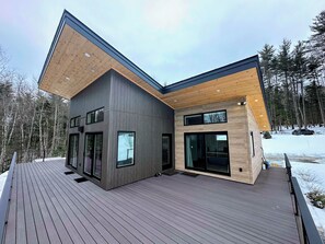 Una casa moderna a due piani con una veranda in legno, ampie finestre e un paesaggio innevato.
