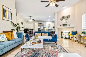 A modern living room with a blue sofa, a coffee table with a fruit platter, and a colorful rug. - Relaxing 4BR Retreat w/ Refreshing Pool (Indio)