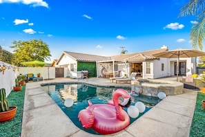 A backyard with a swimming pool, a flamingo float, and a patio area with outdoor furniture. - Relaxing 4BR Retreat w/ Refreshing Pool (Indio)