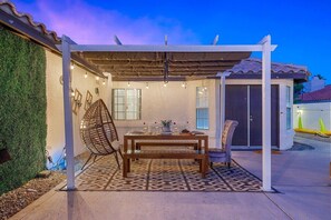 An outdoor patio with a wooden table set for dining, surrounded by chairs and a pergola. - Relaxing 4BR Retreat w/ Refreshing Pool (Indio)
