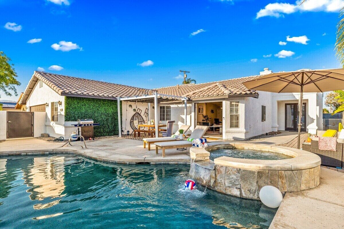 A backyard with a swimming pool, a hot tub, and a patio area with outdoor furniture.