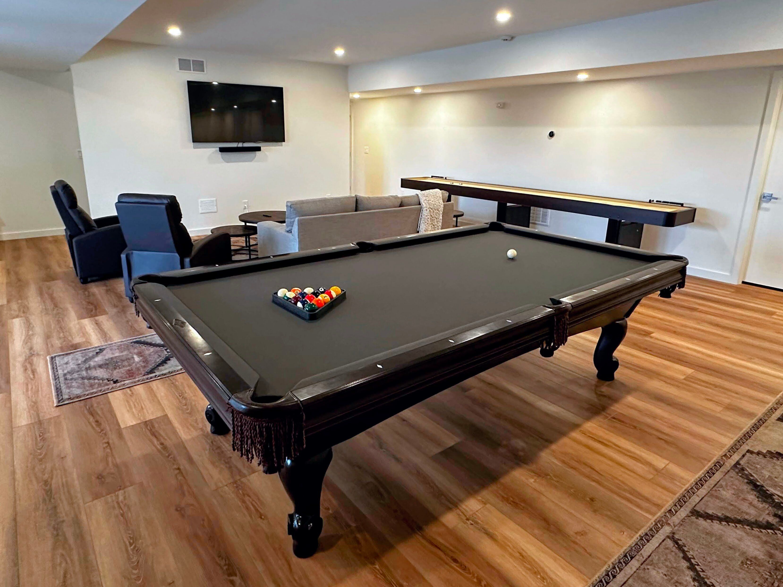 A pool table with balls, a sofa, a TV, and a door in a room with wooden flooring.