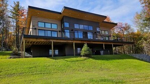 Ein modernes, zweistöckiges Haus mit großzügigem Balkon, umgeben von einem Rasen und Bäumen.