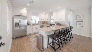 A modern kitchen with white cabinetry, stainless steel appliances, and a central island with bar stools. - 125 Harbor Bluff Dr (Largo)