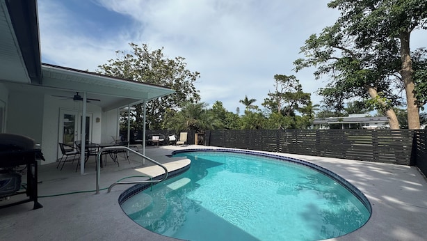 A swimming pool with a curved edge, surrounded by a patio area with chairs and a table. - Desoto (Bradenton)