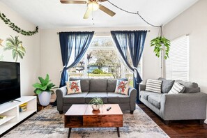 A living room with a grey sofa, a wooden coffee table, a TV, and a plant. - Orlando Airport Vacation Home Pet Friendly (Orlando)