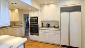 Une cuisine moderne avec des meubles blancs, un four encastré, un four à micro-ondes et un réfrigérateur.