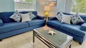 A living room with two blue sofas, a glass coffee table, and a yellow lamp. - Seaside Escape (Bradenton Beach)
