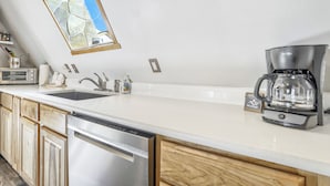 Una cocina moderna con encimera blanca, electrodomésticos de acero inoxidable, armarios de madera, una cafetera y un ventanal con vistas.