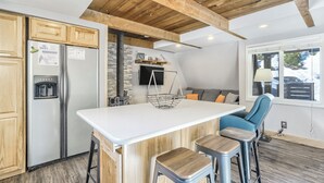 Una cocina con una isla central, armarios de madera, un refrigerador de acero inoxidable y un protector contra salpicaduras de piedra.
