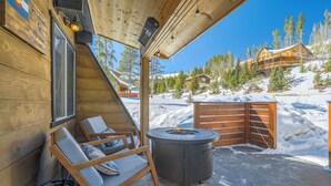 Una cabaña de madera con chimenea, mobiliario exterior y vistas a una montaña nevada.