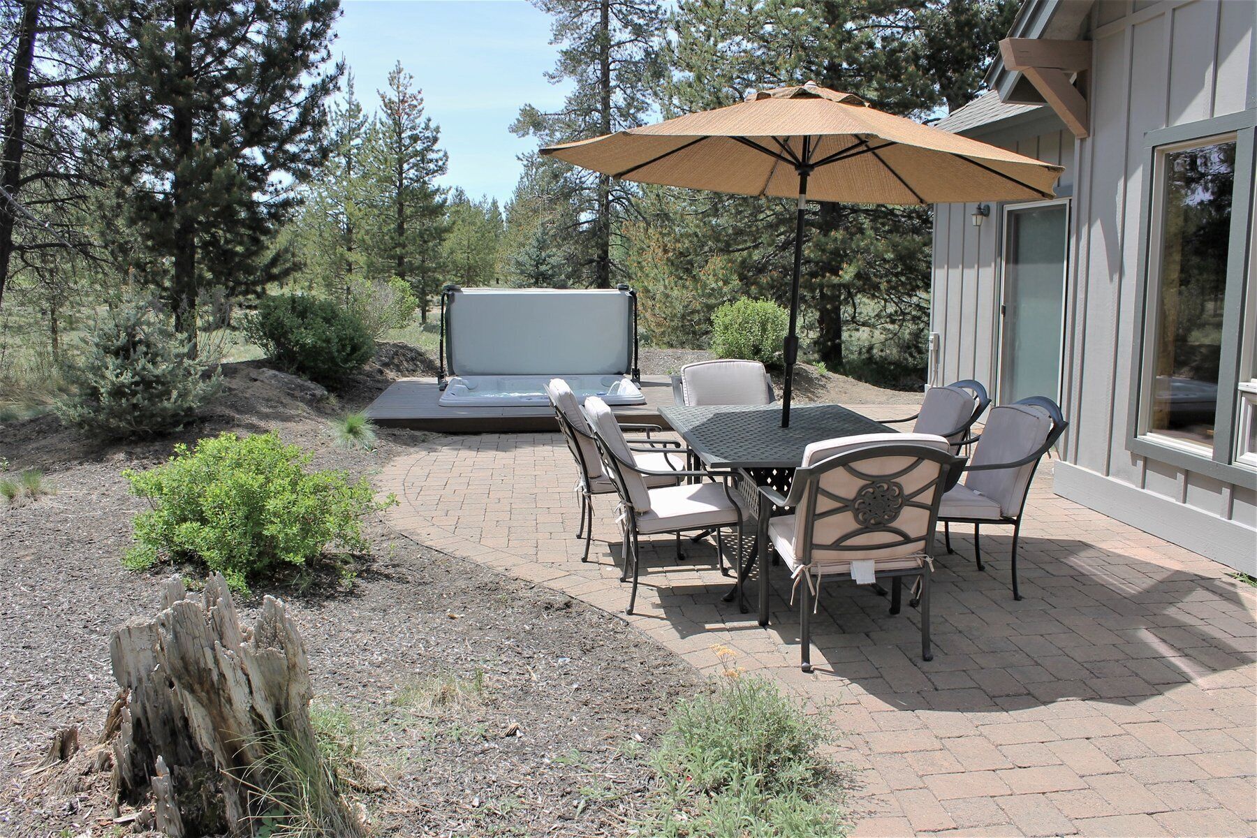 An outdoor patio with a table and chairs, a large umbrella, and a hot tub.