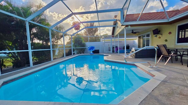 A swimming pool with a glass enclosure, surrounded by outdoor furniture and a covered patio area. - The Salty Pelican (Bradenton)