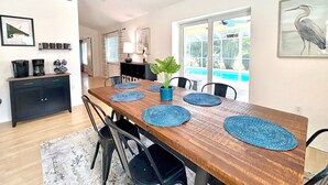 A dining area with a wooden table, blue placemats, black chairs, a potted plant, and a view of a swimming pool through a glass door. - The Salty Pelican (Bradenton)