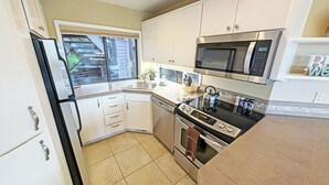 Cucina compatta con mobili bianchi, frigorifero in acciaio inossidabile, microonde, forno e lavastoviglie.
