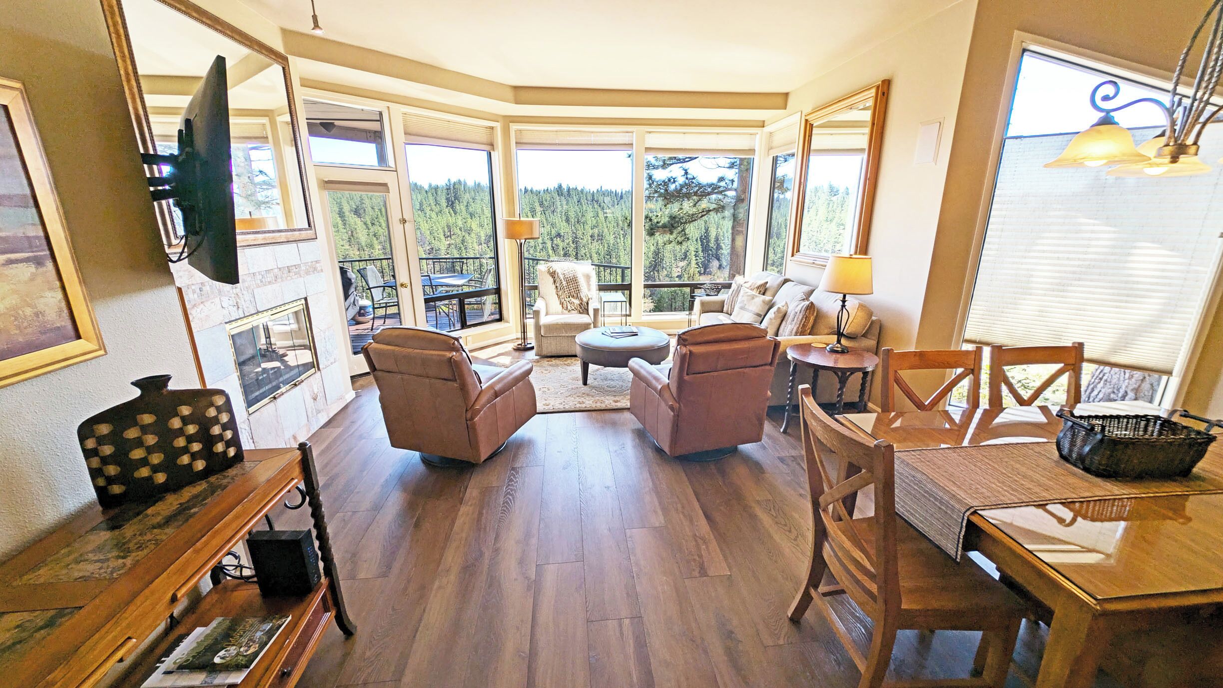 A spacious living room with a fireplace, large windows, and a dining area with wooden furniture.