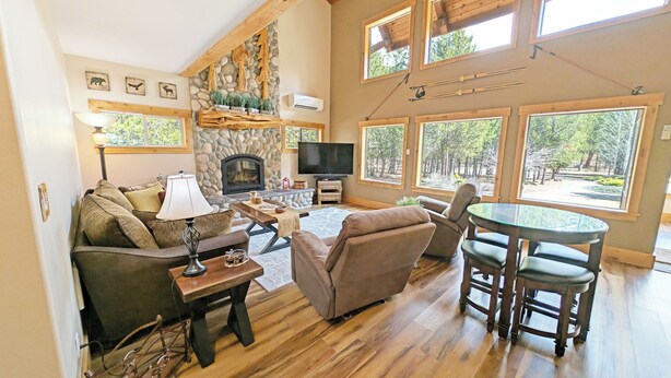 A cozy living room with a stone fireplace, a television, and large windows offering a view of the outdoors. - Aspen Place River Access & Ping Pong (Bend)