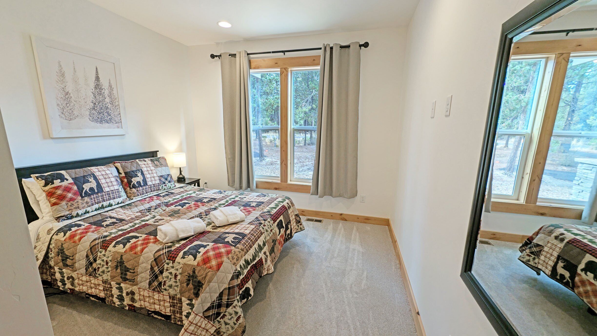 A bedroom with a large bed, a window with curtains, a headboard with a painting, and a mirror on the wall.