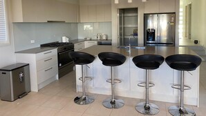 A modern kitchen with a central island, stainless steel appliances, and bar stools. - Spacious Family & Group Retreat | Sleeps 10 | 3 Baths | free parking  (North Kellyville)