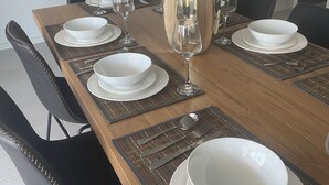 A dining table set with white plates, bowls, and cutlery, accompanied by a vase of flowers. - Spacious Family & Group Retreat | Sleeps 10 | 3 Baths | free parking  (North Kellyville)