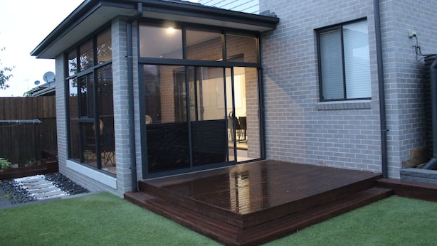 A modern house with a glass-enclosed patio and a wooden deck. - Spacious Family & Group Retreat | Sleeps 10 | 3 Baths | free parking  (North Kellyville)