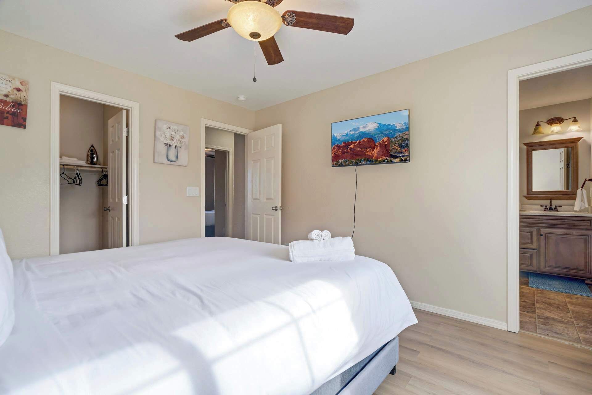A hotel room with a bed, a ceiling fan, a painting, and a bathroom visible through an open door.