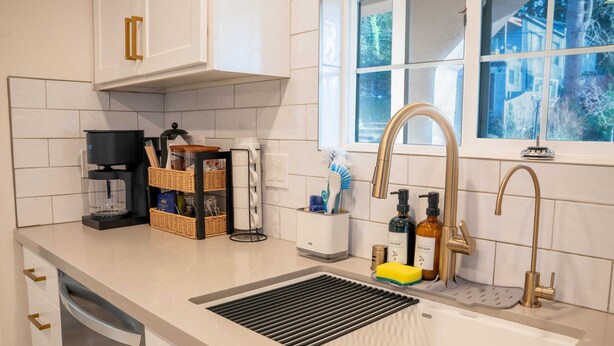 Cozinha moderna com pia de aço inoxidável, cafeteira e janela com vista para o exterior.