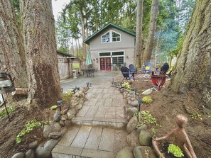 A building with a green roof and a red door, surrounded by trees and a stone pathway leading to outdoor seating.
