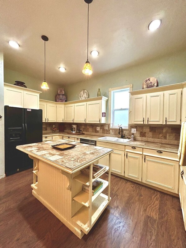 A kitchen with a central island, white cabinetry, a black refrigerator, and pendant lighting.