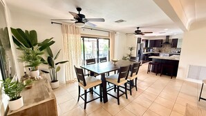 A modern kitchen with dark cabinets, a central island, and a dining area with a table and chairs. - Waterfront, Pool + South Florida Vibes - Perfect! (Pompano Beach)