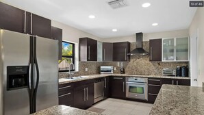 A modern kitchen with dark cabinets, stainless steel appliances, granite countertops, and a built-in oven. - Waterfront, Pool + South Florida Vibes - Perfect! (Pompano Beach)