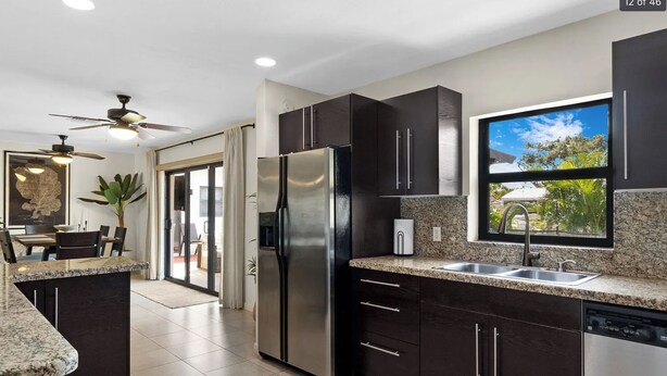 A modern kitchen with dark cabinetry, stainless steel appliances, a granite countertop, and a window with a view of greenery. - Waterfront, Pool + South Florida Vibes - Perfect! (Pompano Beach)