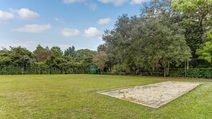 A grassy field with a sandpit and trees in the background. - 10D Amelia Landings (Fernandina Beach)