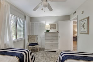A bedroom with two beds, a ceiling fan, a dresser, a chair, and a door leading to another room. - 10D Amelia Landings (Fernandina Beach)