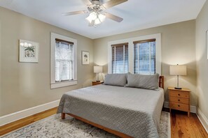 A bedroom with a bed, two bedside tables, a ceiling fan, and two windows with blinds. - 114 S 6th Street (Fernandina Beach)